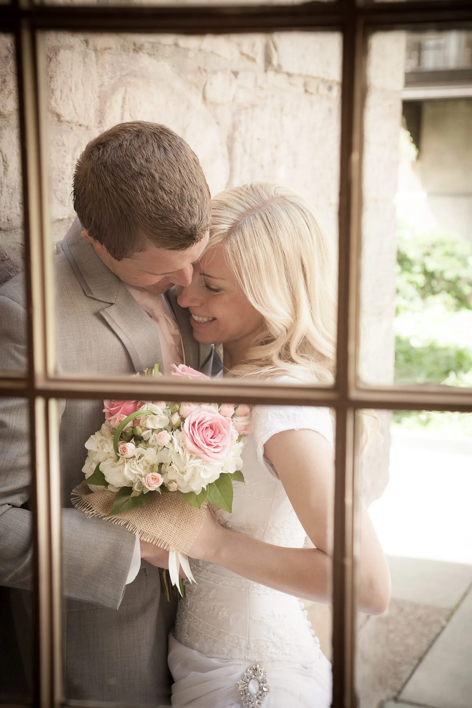 Bride and groom framed by a window, holding a pastel bouquet