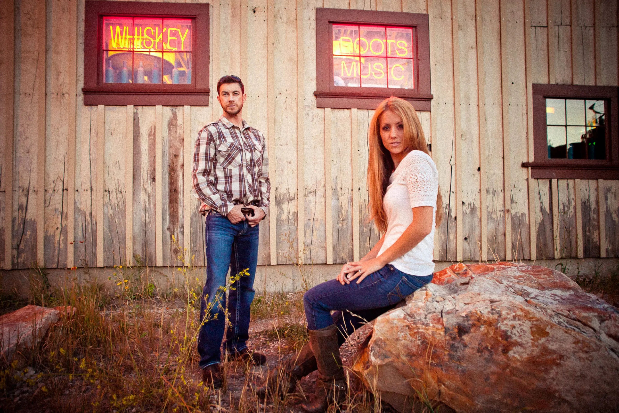 Engaged couple sitting on a rock beside a rustic red barn