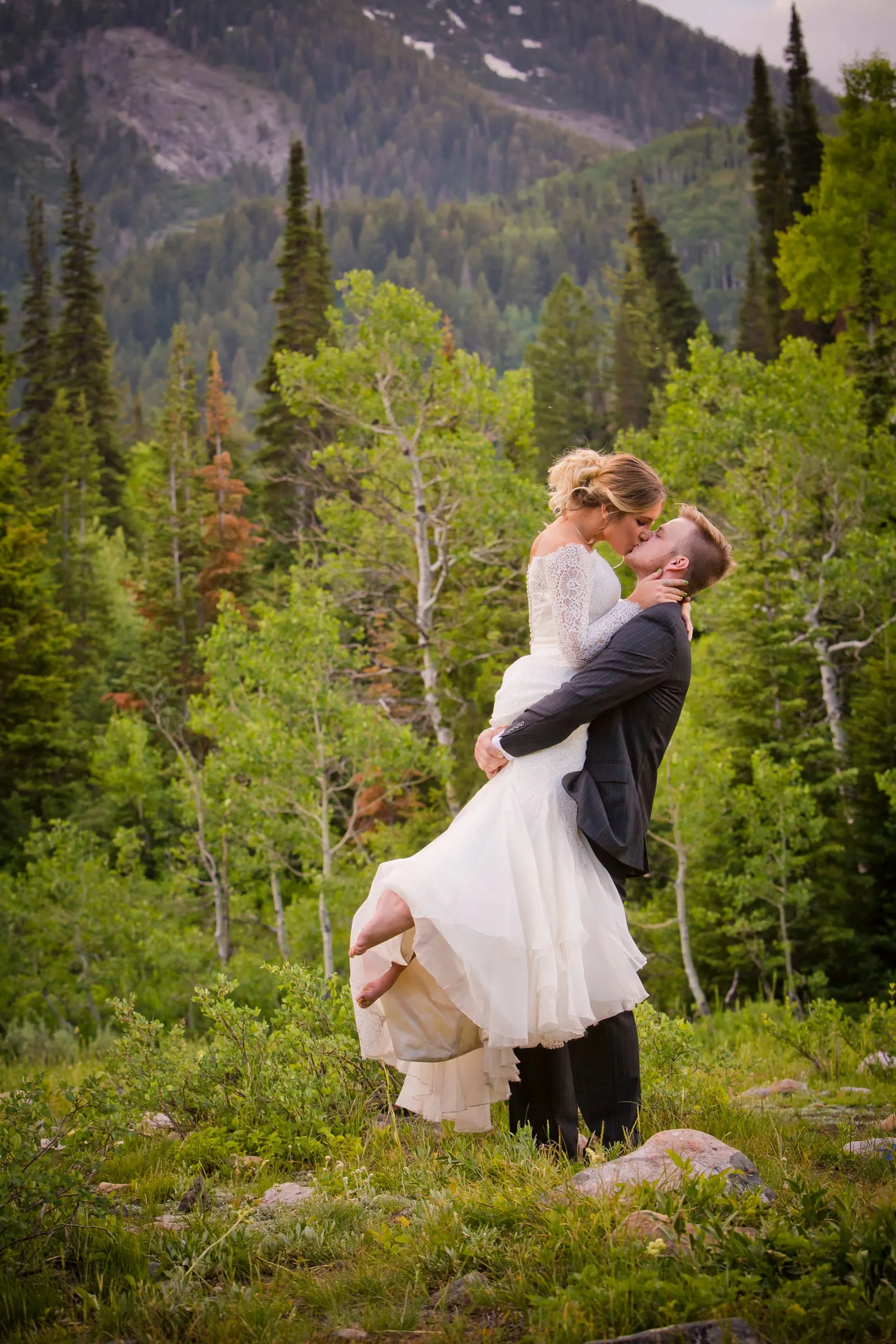 Groom lifting his bride among aspen trees with mountains behind