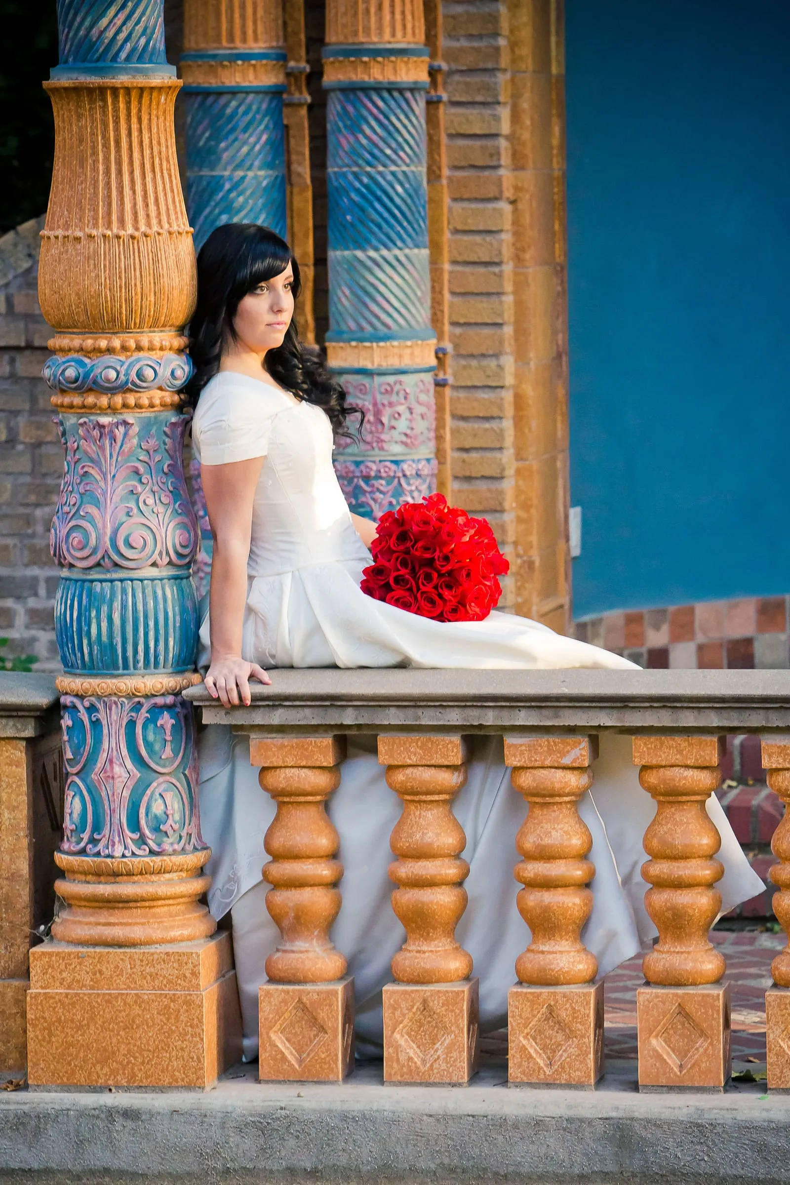 Bride holding red roses on an ornate, colorful balcony