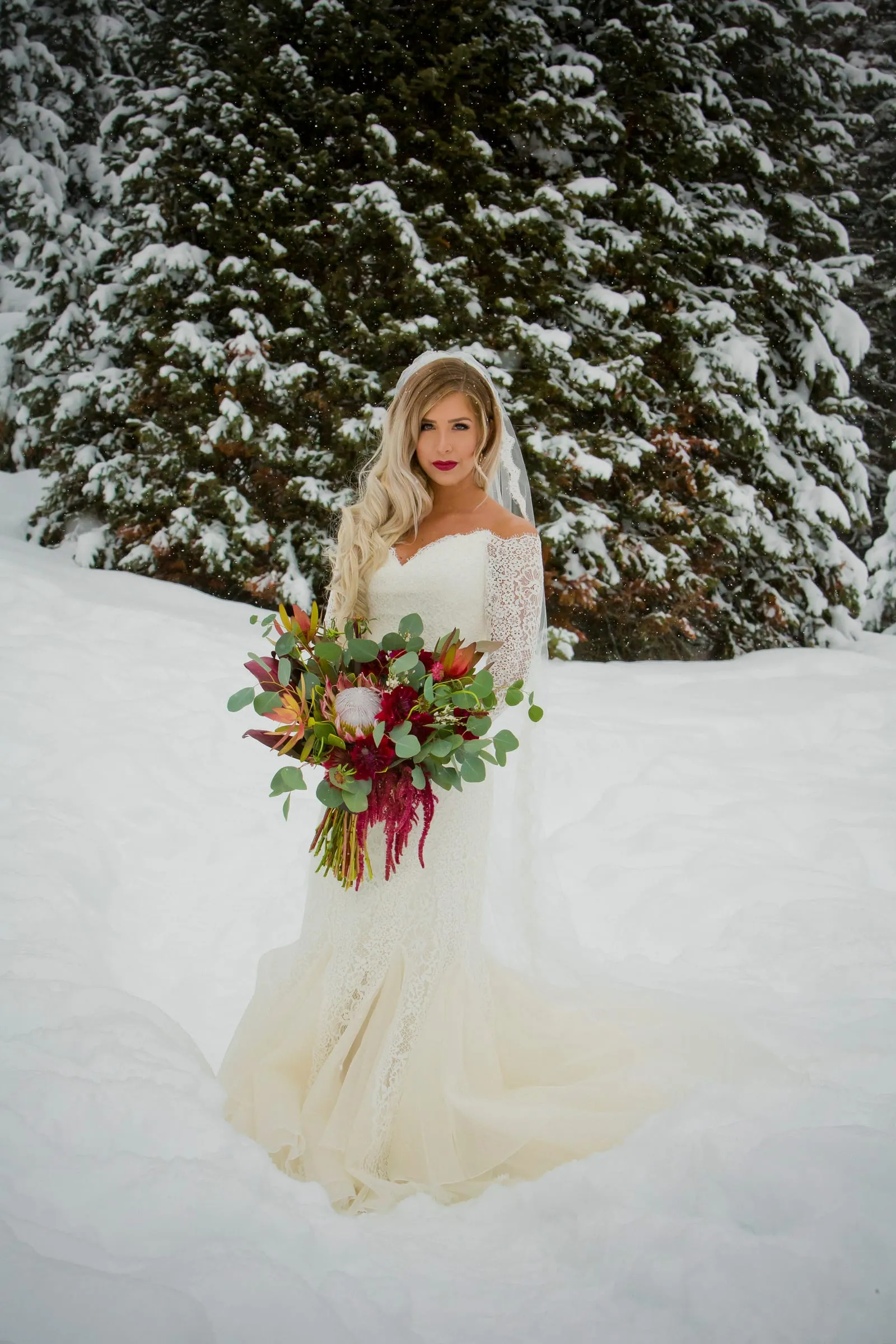 Bride in a long veil standing in a snowy pine forest