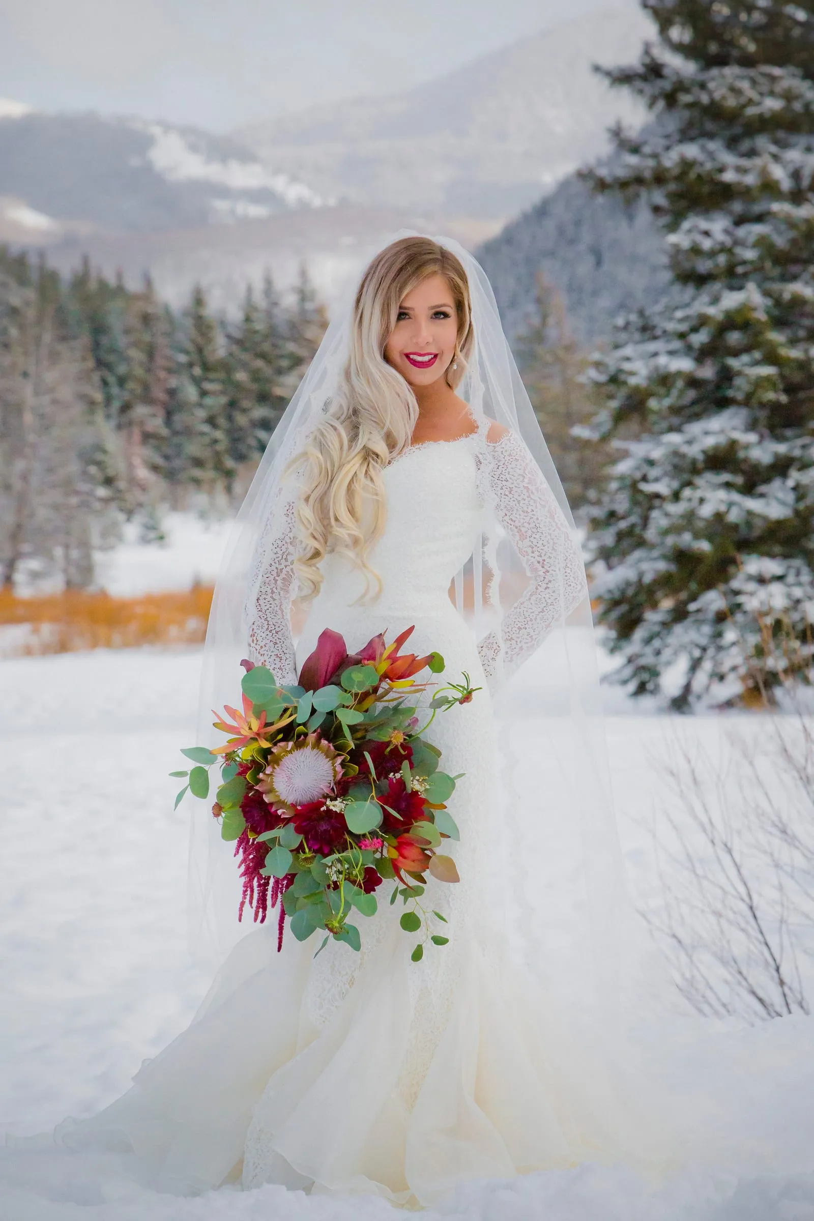 Winter bride holding a red bouquet in a snowy mountain meadow