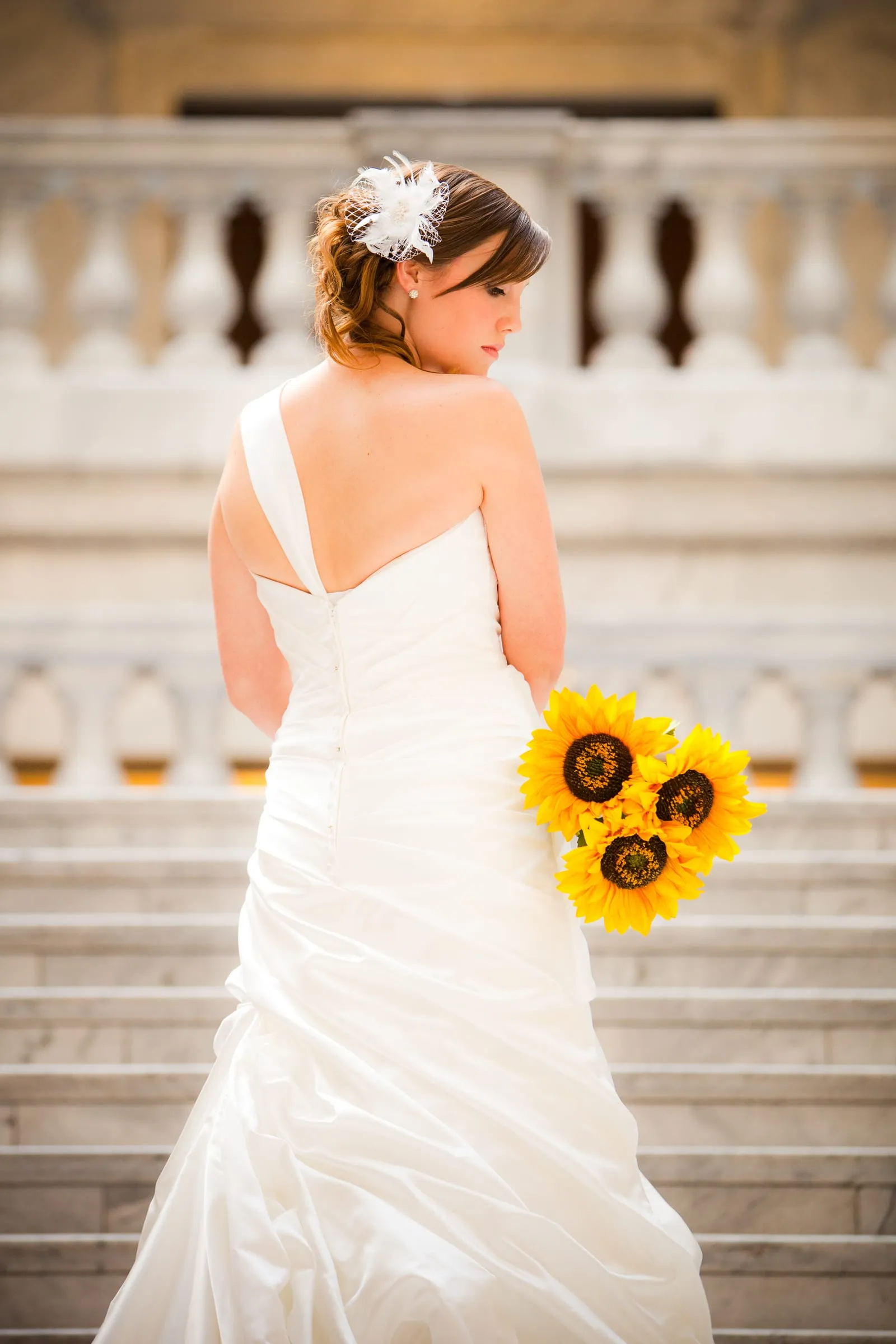 Bride seen from behind holding sunflowers on white stone stairs