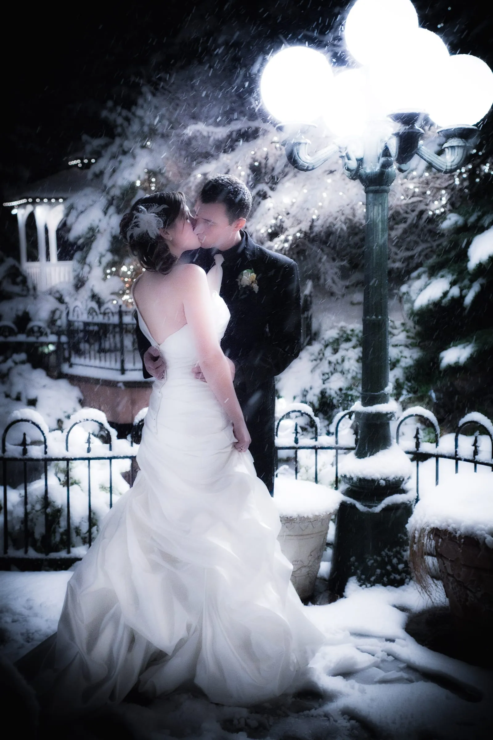 Bride and groom kissing under a lamppost on a snowy night