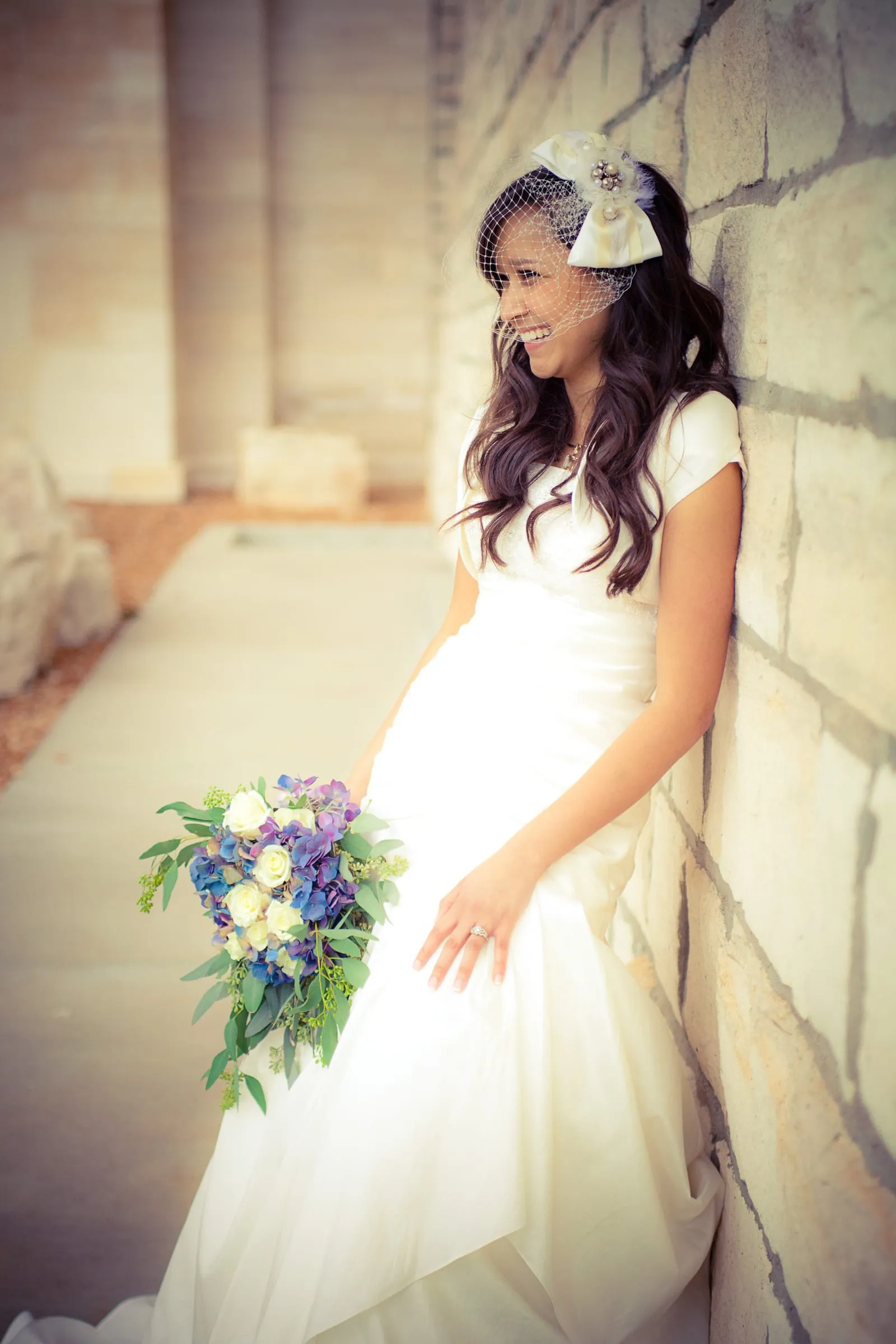 Bride in a vintage hat holding a bouquet against a white wall