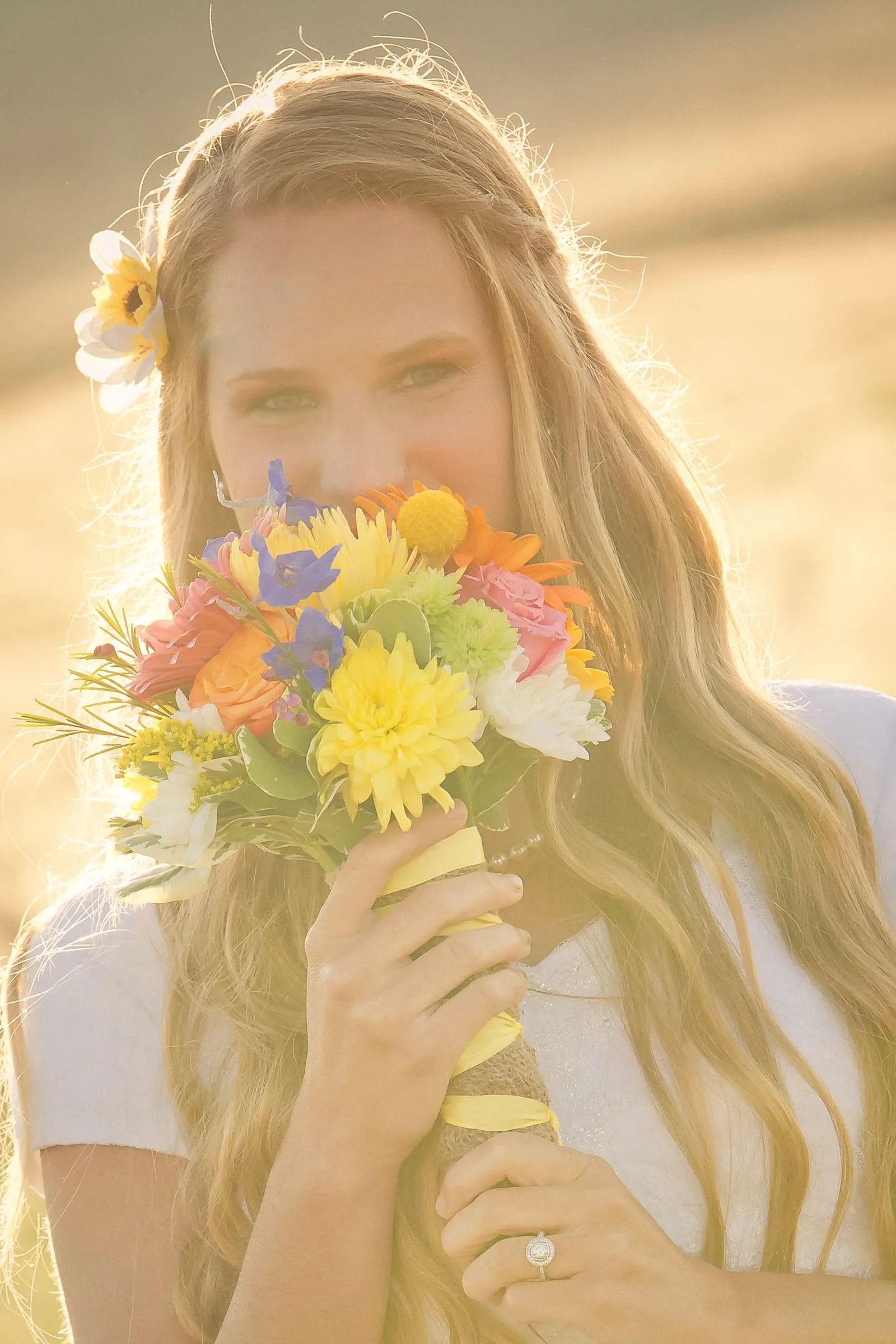 Bride smiling over a bright wildflower bouquet in golden light