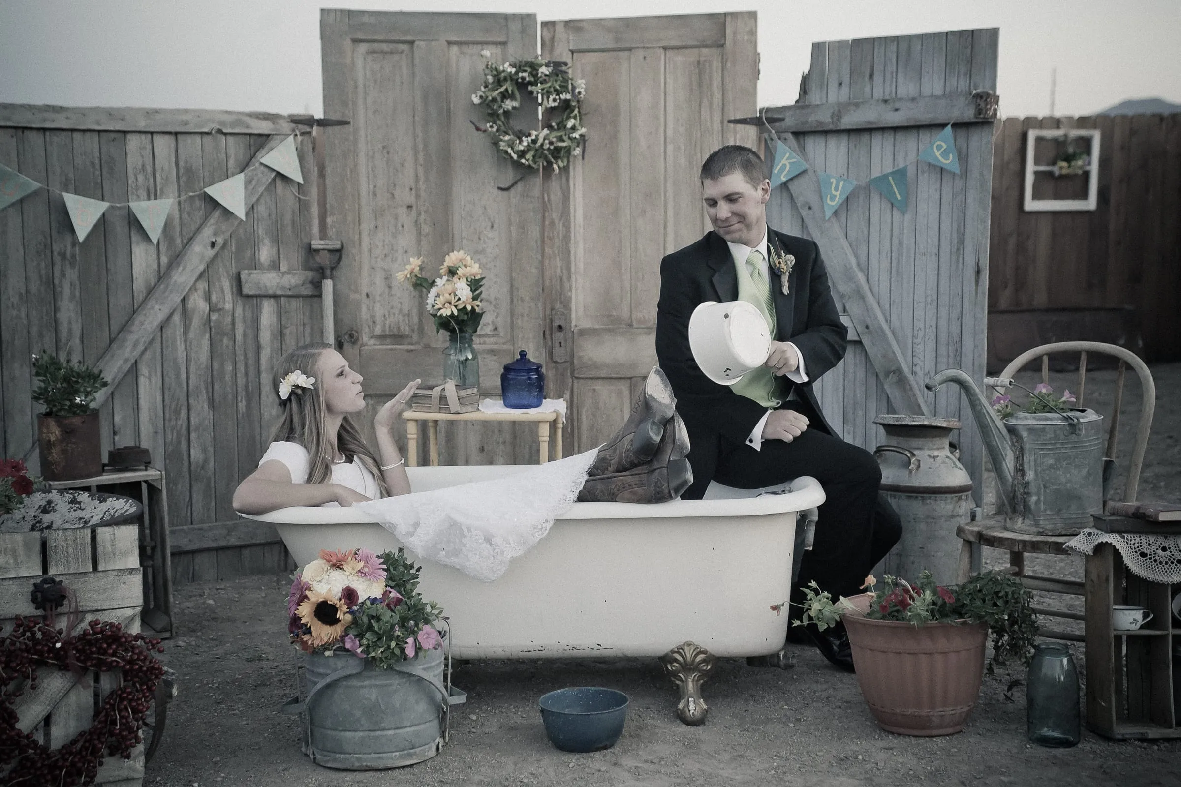 Black-and-white portrait of a bride and groom with a vintage clawfoot tub in a rustic barn