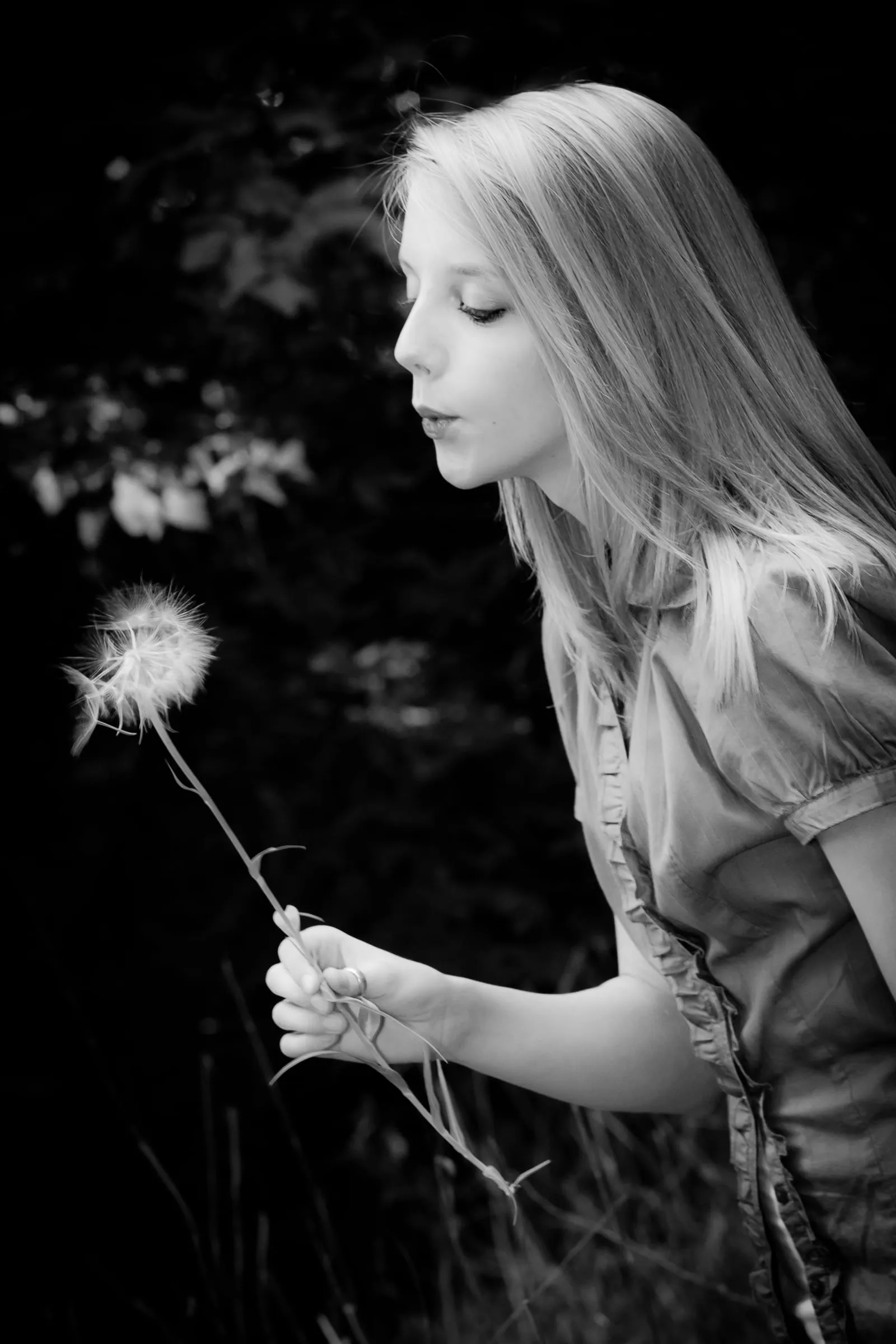 Black-and-white portrait of a woman blowing a dandelion