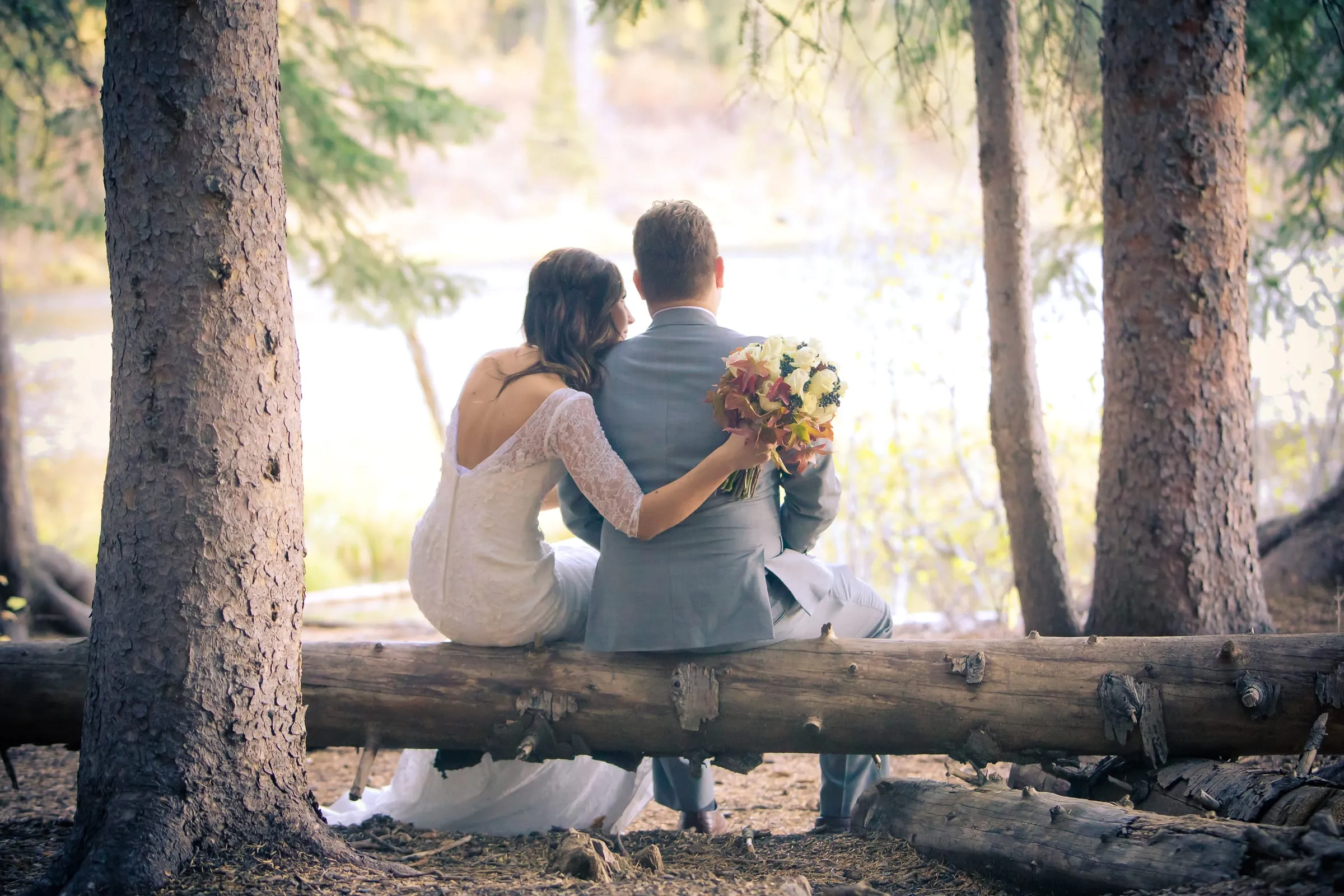 Bride and groom sitting close on a fallen log in a sunlit forest