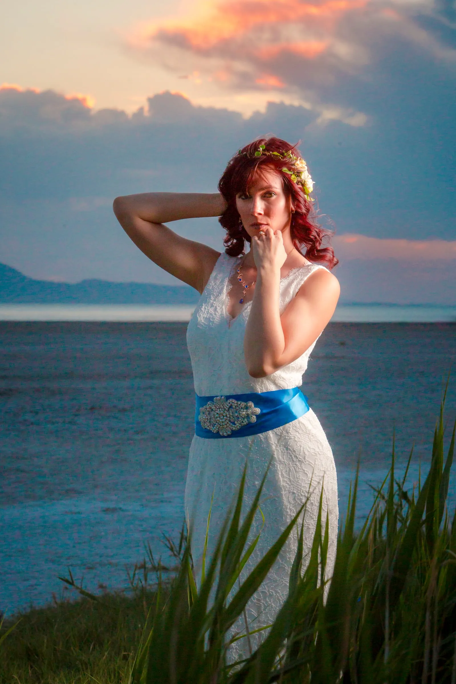 Bride with a blue sash posing by the lake at sunset