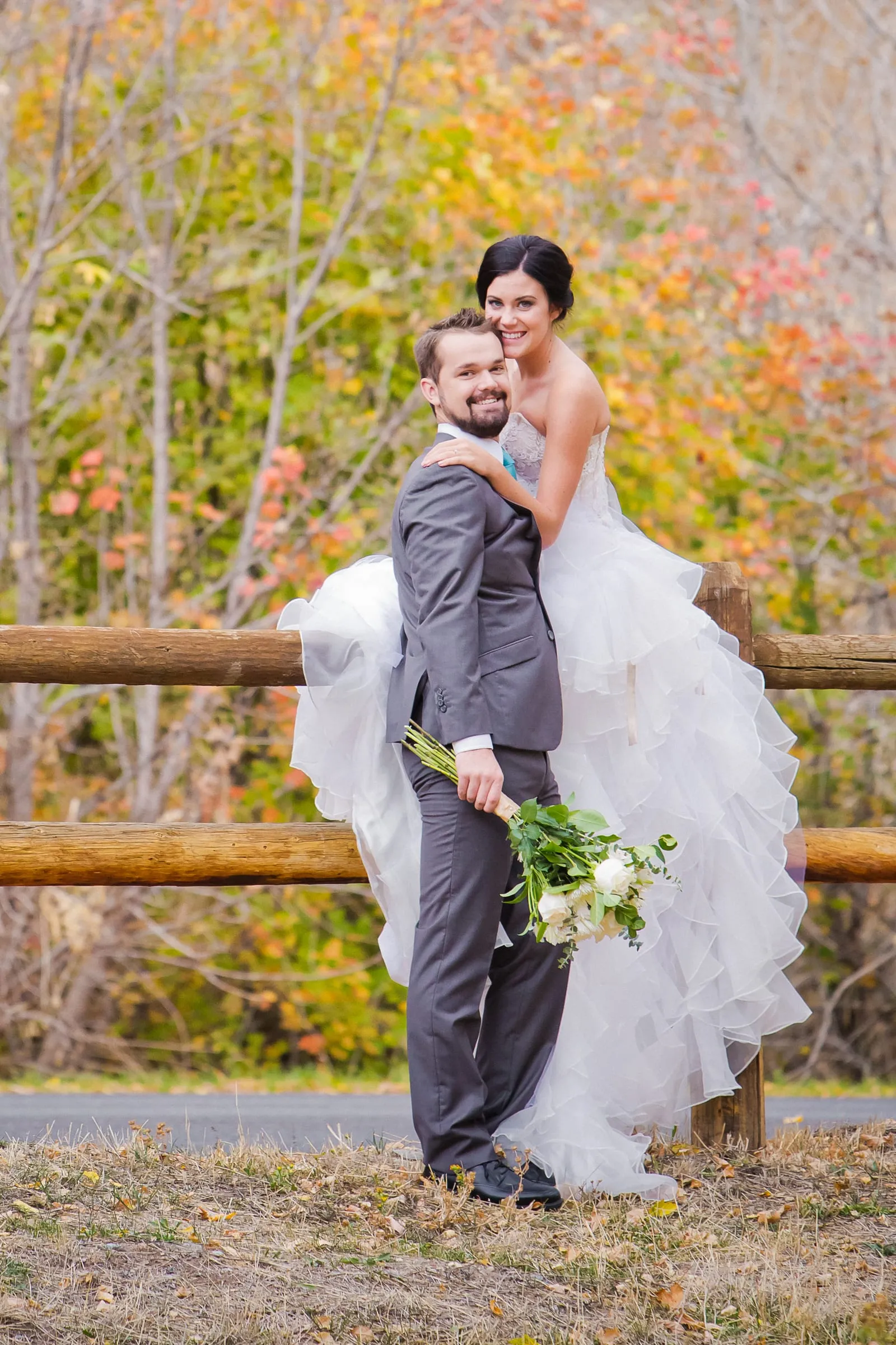 Groom holding his bride by a wooden fence in autumn color