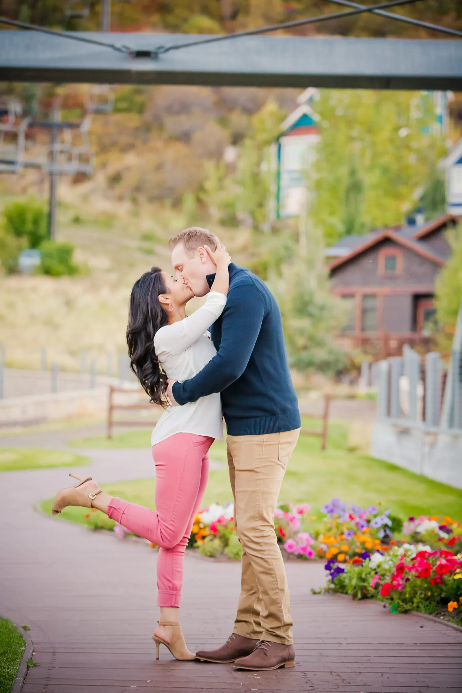 Couple kissing beside a flower garden, her foot playfully lifted