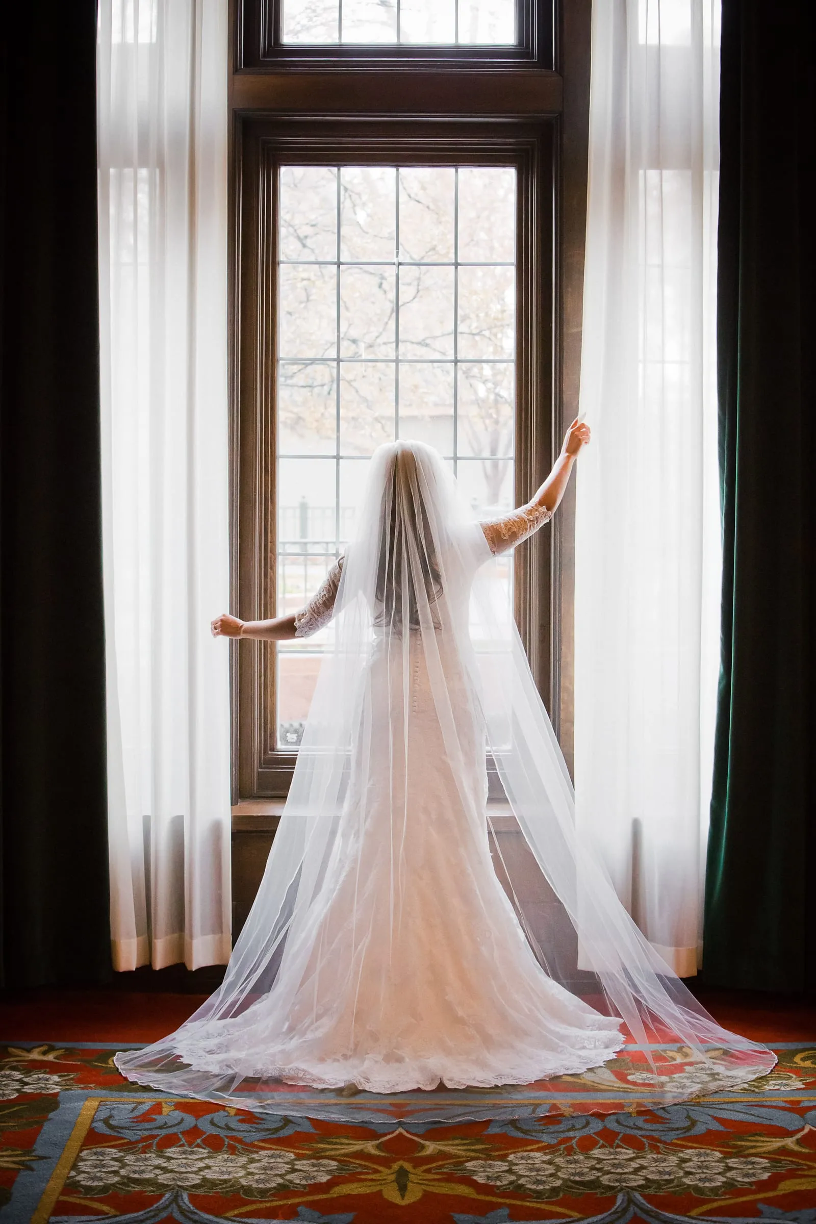 Bride standing by a tall window framed in sheer curtains