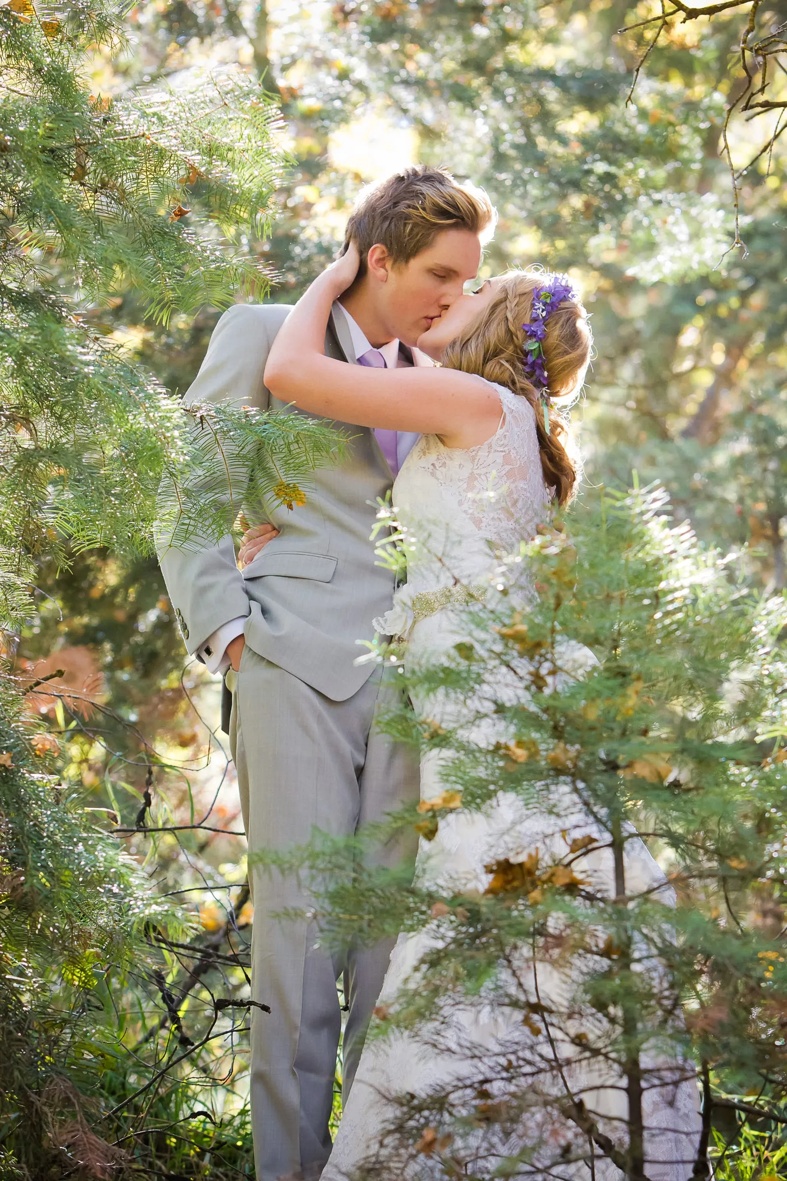 Groom embracing his bride among pine branches