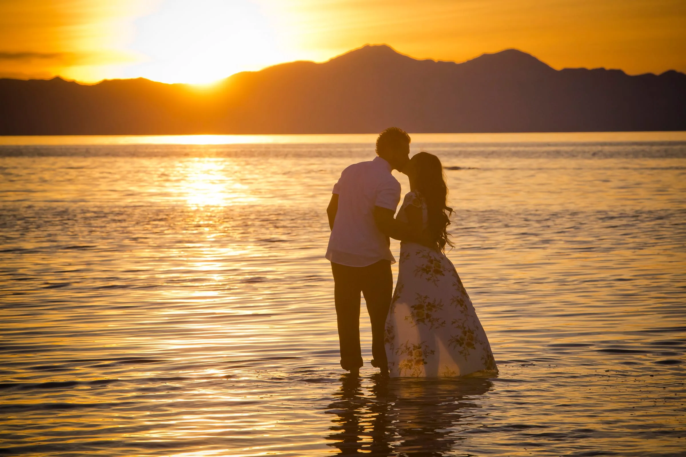 Engaged couple silhouetted at sunset, standing together in a calm Utah lake