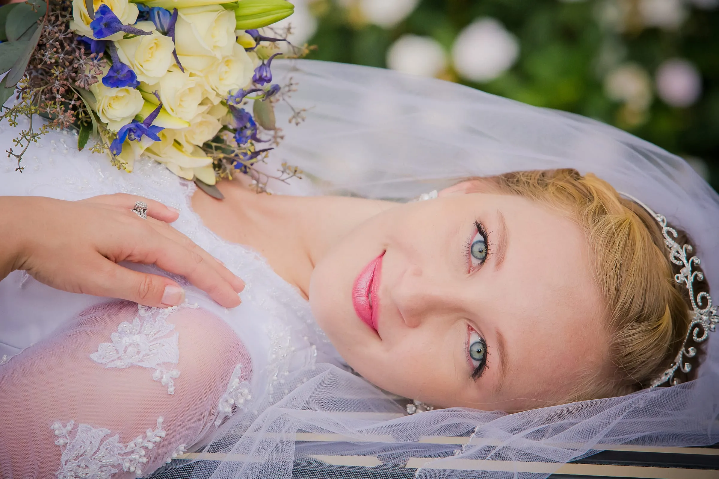 Bride lying back in her veil, smiling, with flowers beside her