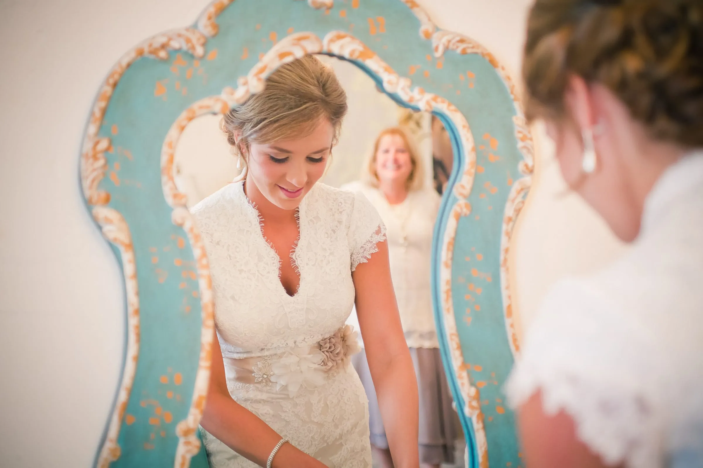 Bride checking her reflection in an ornate teal mirror