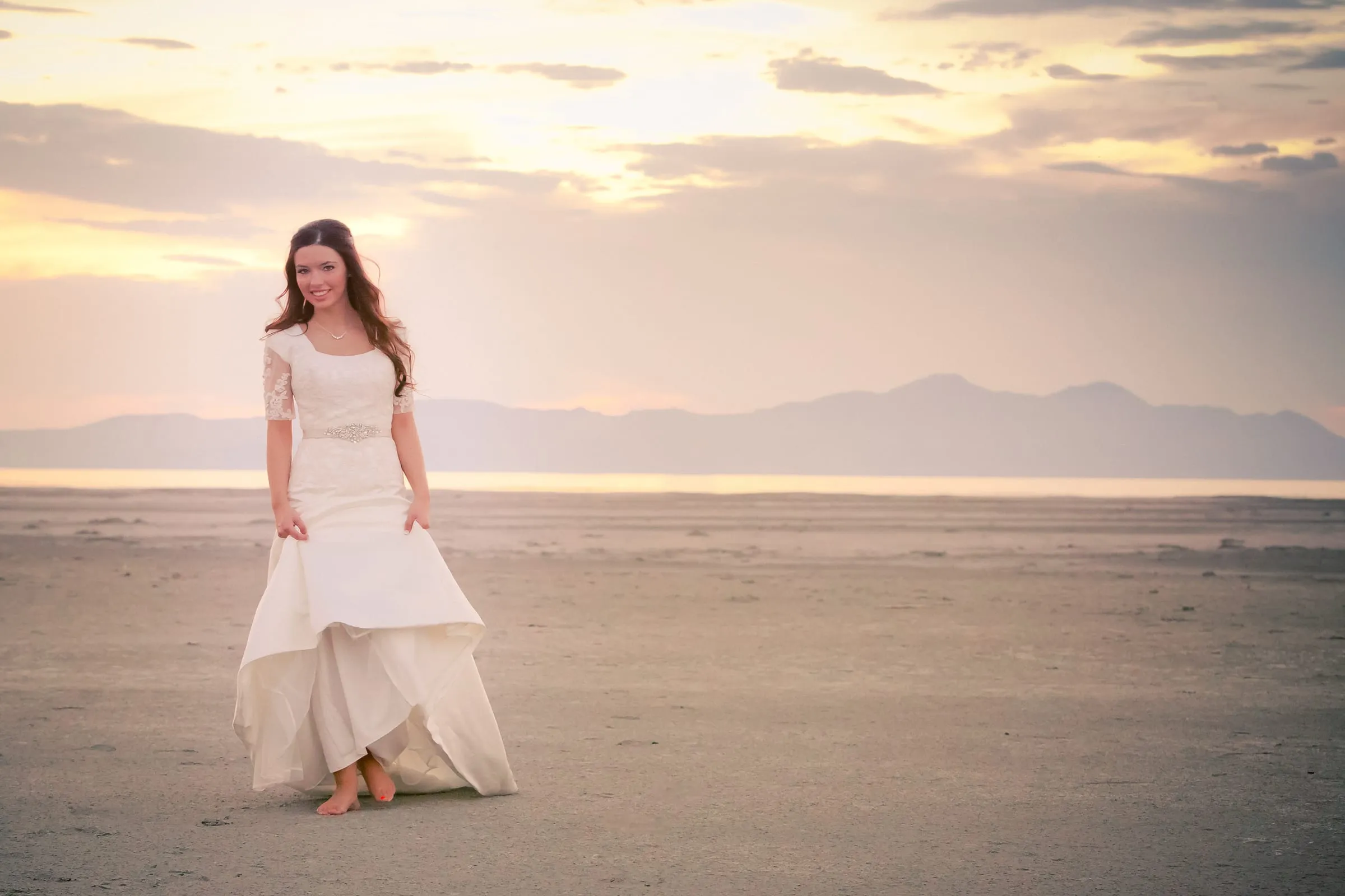 Bride walking across open salt flats at sunset with mountains on the horizon