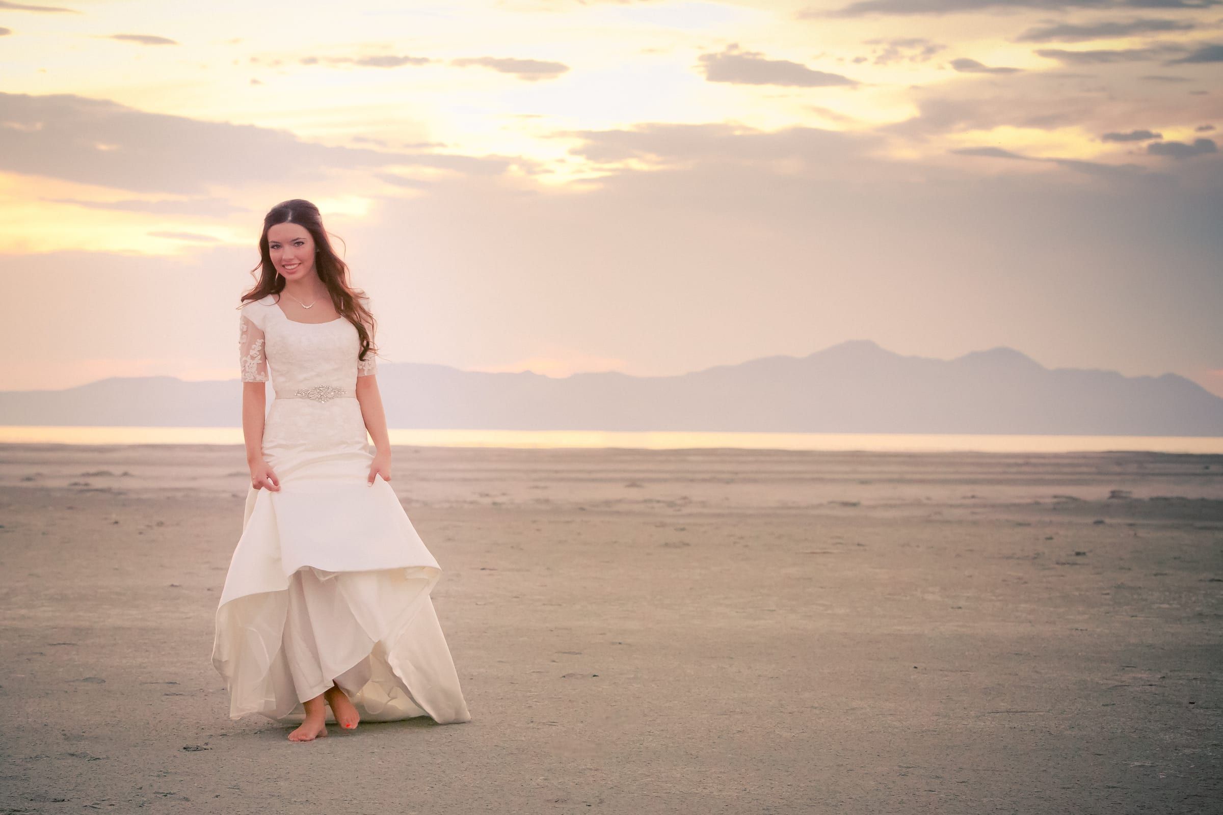Bride walking across open salt flats at sunset with mountains on the horizon