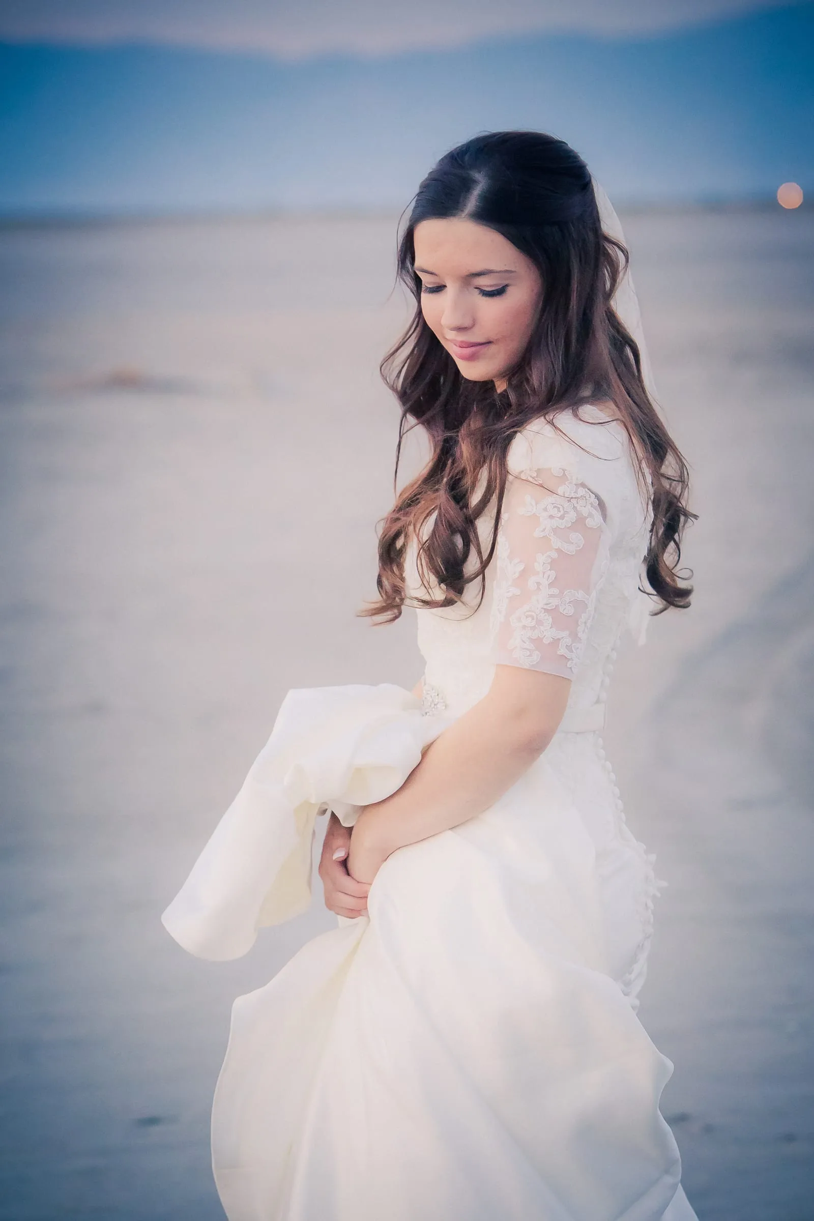 Bride in a lace gown lifting her skirt on the salt flats
