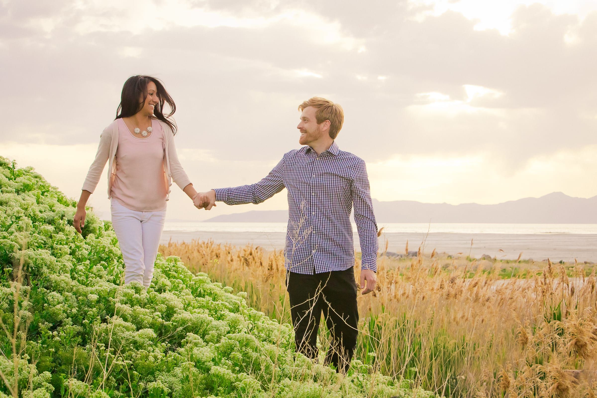 Couple walking hand in hand along a grassy hillside above a lake