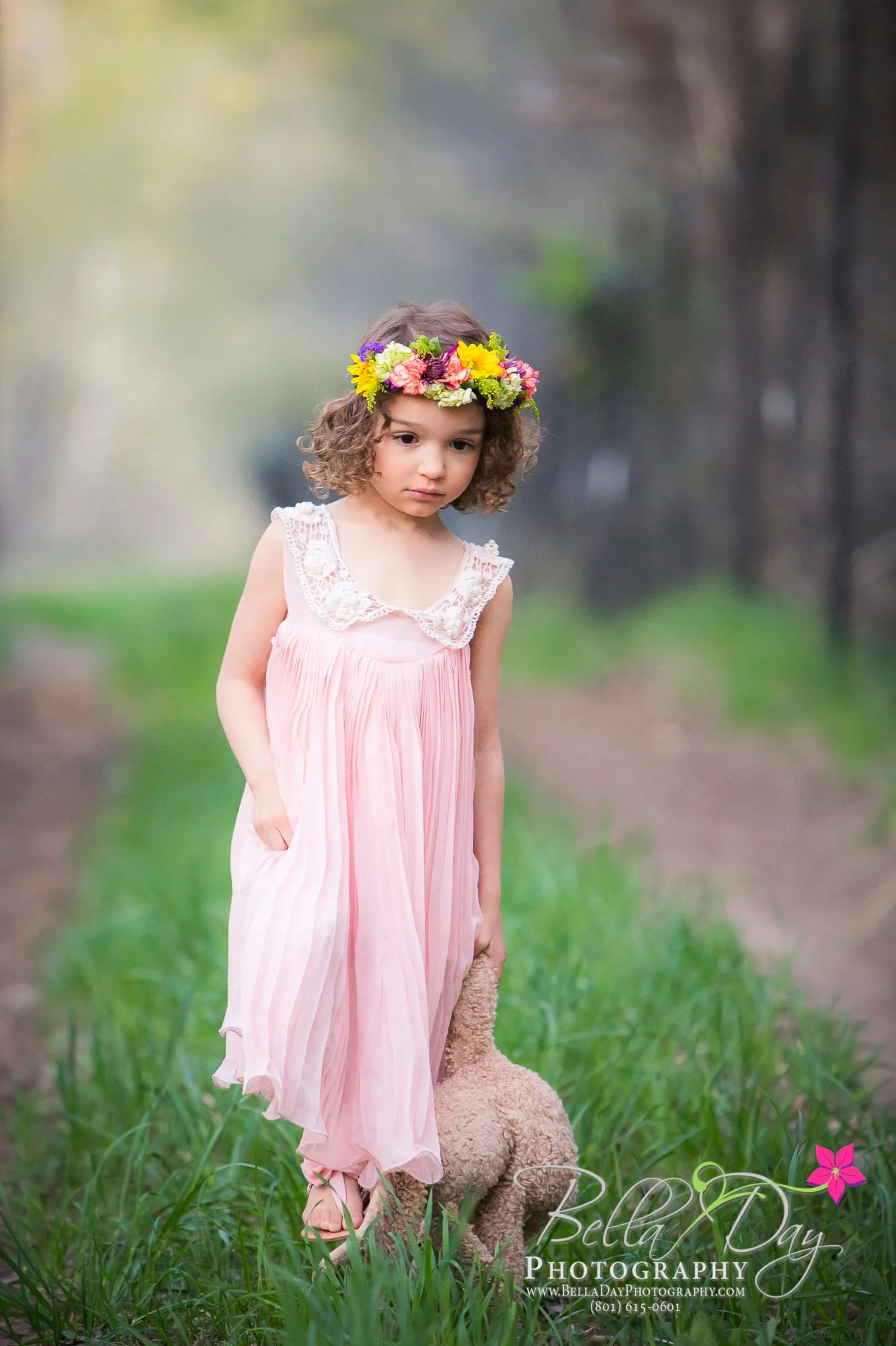 Little girl in a pink dress and flower crown on a garden path